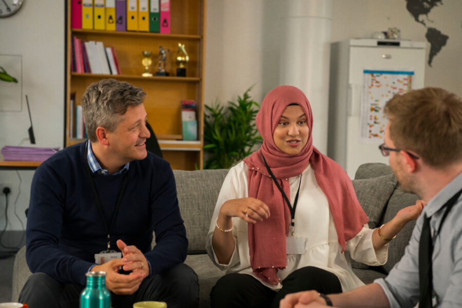 Three teachers sat on sofas having a conversation in a school staff room.